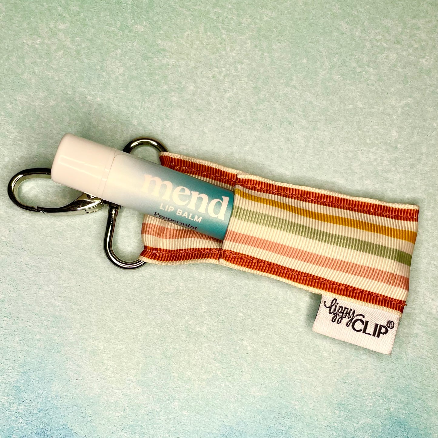 Mend Peppermint Lip Balm and a striped Lippy Clip lip balm holder featured in the spring 2024 Millions of Peaches Box
